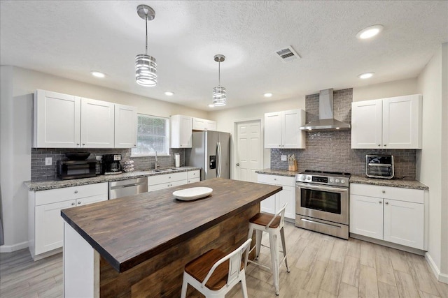 11503 Davidson Rd, Beaumont, TX 77705 - kitchen featuring appliances with stainless steel finishes, wall chimney range hood, tasteful backsplash, white cabinetry, and hanging light fixtures