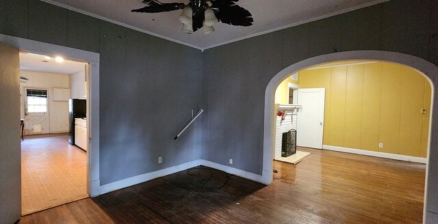 unfurnished room with a brick fireplace, ceiling fan, wood-type flooring, and ornamental molding