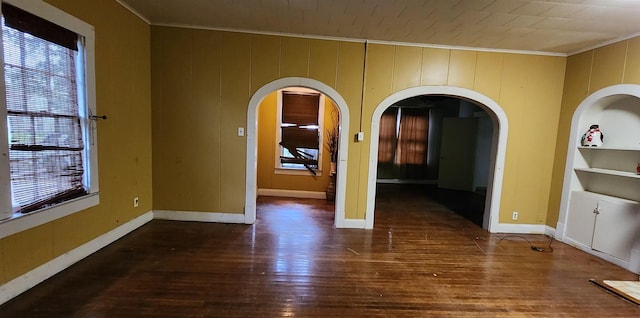 unfurnished room with built in shelves, a wealth of natural light, dark hardwood / wood-style flooring, and ornamental molding