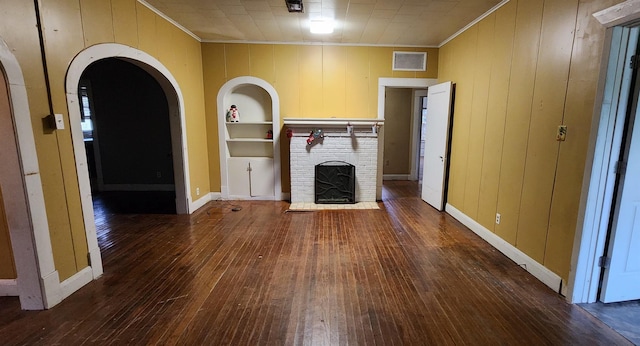 unfurnished living room with built in shelves, dark hardwood / wood-style flooring, a brick fireplace, and crown molding