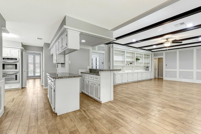 kitchen featuring double oven, light hardwood / wood-style flooring, dark stone countertops, white cabinets, and a kitchen island