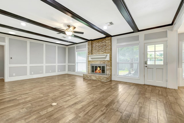 unfurnished living room featuring ceiling fan, beam ceiling, light wood-type flooring, and a brick fireplace