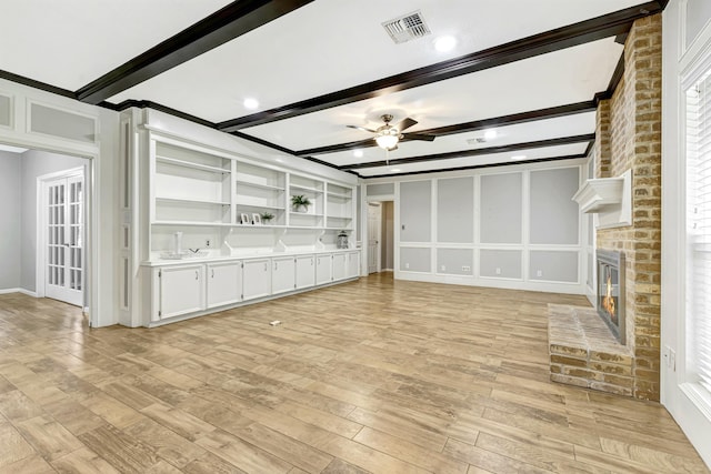 unfurnished living room featuring ceiling fan, a fireplace, beamed ceiling, and light hardwood / wood-style flooring