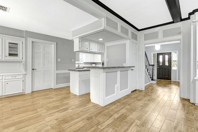 kitchen with kitchen peninsula, ornamental molding, dark stone counters, light hardwood / wood-style flooring, and white cabinets