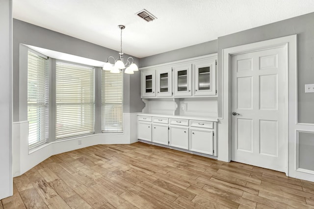 unfurnished dining area with light wood-type flooring, a textured ceiling, and an inviting chandelier