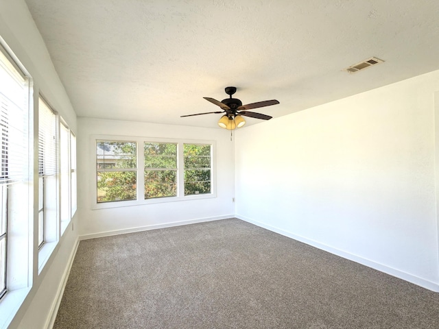 spare room featuring ceiling fan, dark carpet, a textured ceiling, and a healthy amount of sunlight