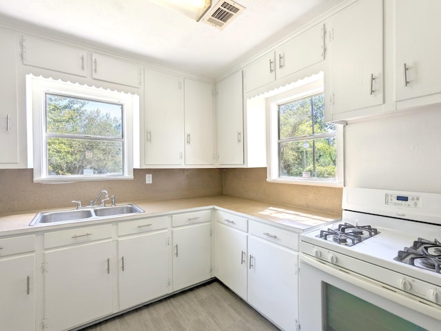 kitchen featuring sink, white range with gas stovetop, backsplash, light hardwood / wood-style floors, and white cabinets