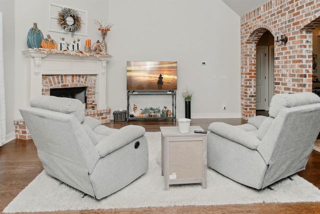 living room with wood-type flooring, lofted ceiling, and a brick fireplace