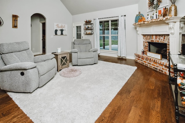 living room featuring vaulted ceiling, a brick fireplace, and dark wood-type flooring