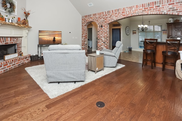 living room with lofted ceiling, a brick fireplace, dark hardwood / wood-style flooring, brick wall, and a chandelier