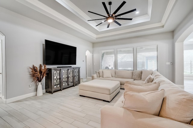 living room with ceiling fan, crown molding, light wood-type flooring, and a raised ceiling