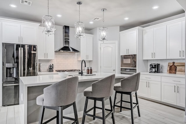 kitchen with stainless steel appliances, wall chimney exhaust hood, an island with sink, and white cabinetry