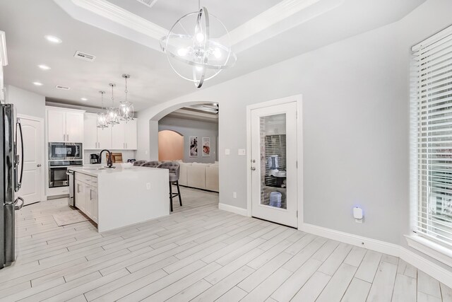 kitchen with pendant lighting, a raised ceiling, a kitchen island with sink, white cabinets, and appliances with stainless steel finishes