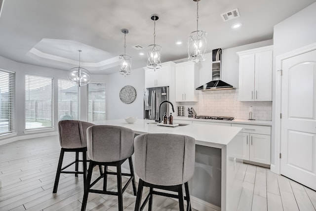 kitchen featuring wall chimney exhaust hood, decorative light fixtures, a raised ceiling, a breakfast bar, and a kitchen island with sink