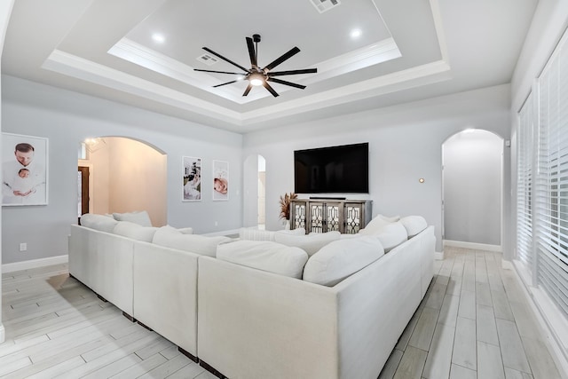 living room with ceiling fan, light hardwood / wood-style flooring, crown molding, and a tray ceiling