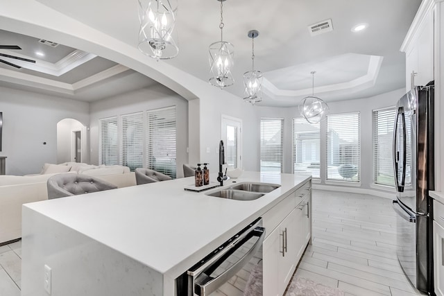 kitchen with white cabinets, dishwasher, black fridge, a raised ceiling, and an island with sink