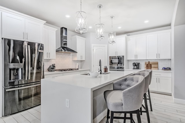 kitchen featuring wall chimney exhaust hood, hanging light fixtures, an island with sink, black refrigerator with ice dispenser, and sink