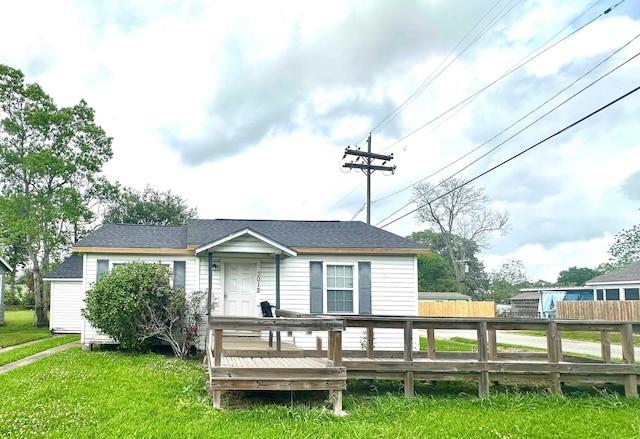 view of front of house with roof with shingles, fence, a front yard, and a deck