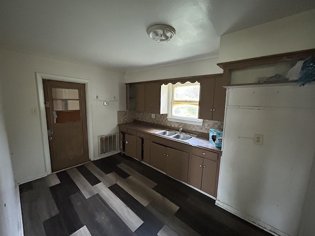 kitchen with dark wood-type flooring, sink, backsplash, and fridge