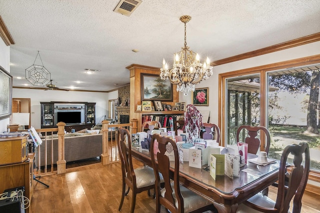 dining area with wood-type flooring, ornamental molding, a textured ceiling, and a brick fireplace