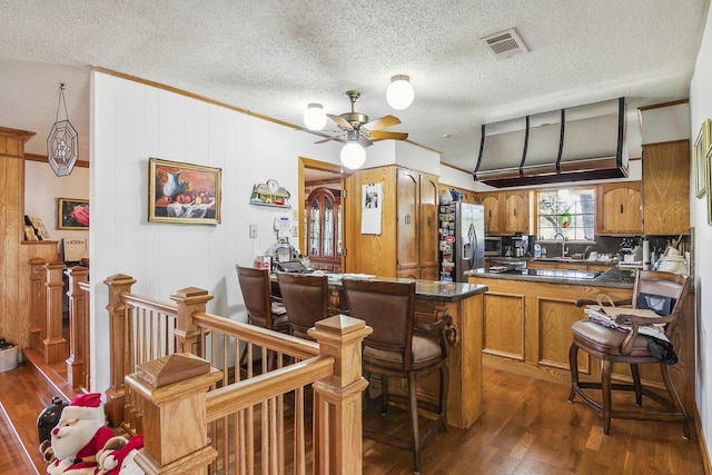 kitchen with dark wood-type flooring, ceiling fan, a kitchen bar, kitchen peninsula, and stainless steel appliances