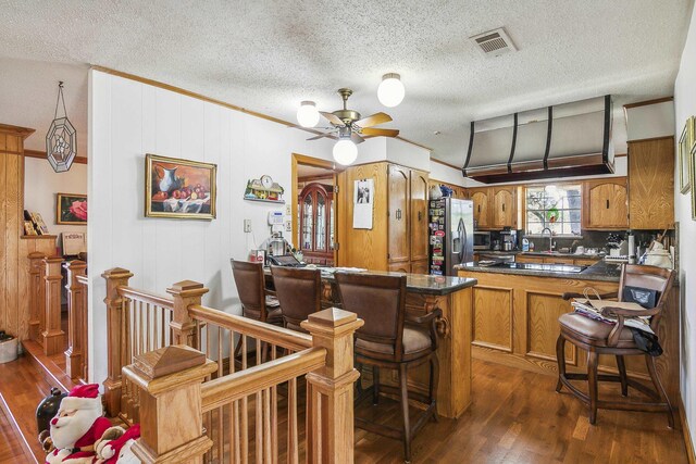 kitchen with dark wood-type flooring, ceiling fan, a kitchen bar, kitchen peninsula, and stainless steel appliances