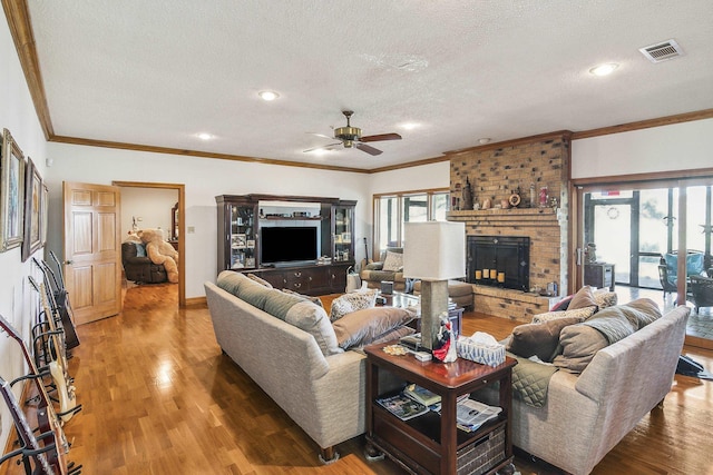 living room featuring a brick fireplace, a textured ceiling, ceiling fan, crown molding, and wood-type flooring