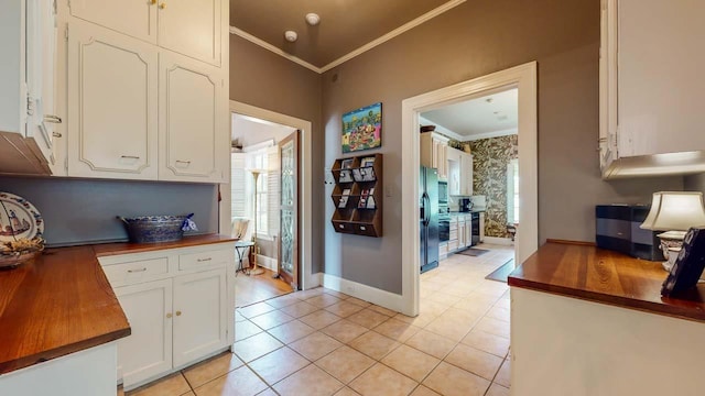 kitchen with black refrigerator, crown molding, butcher block countertops, light tile patterned flooring, and white cabinetry