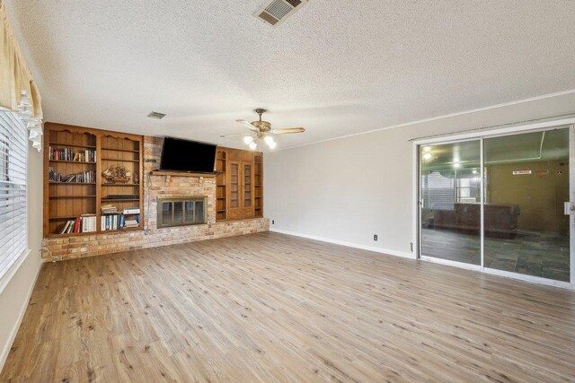 5960 Navajo Trl, Beaumont, TX 77708 - unfurnished living room with a textured ceiling, a brick fireplace, wood finished floors, a ceiling fan, and baseboards