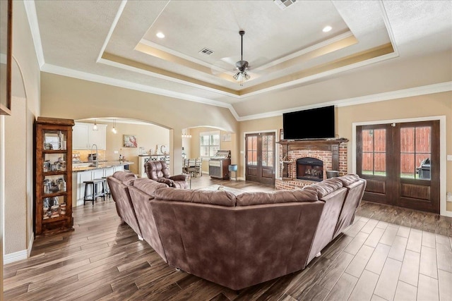3113 Labrador Ln, Port Neches, TX 77651 - living area with visible vents, a fireplace, arched walkways, a tray ceiling, and a ceiling fan