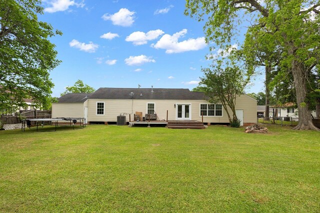 rear view of house with central AC, a deck, a trampoline, and a lawn