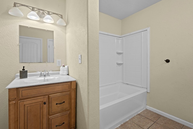 bathroom featuring washtub / shower combination, tile patterned flooring, a textured wall, vanity, and baseboards