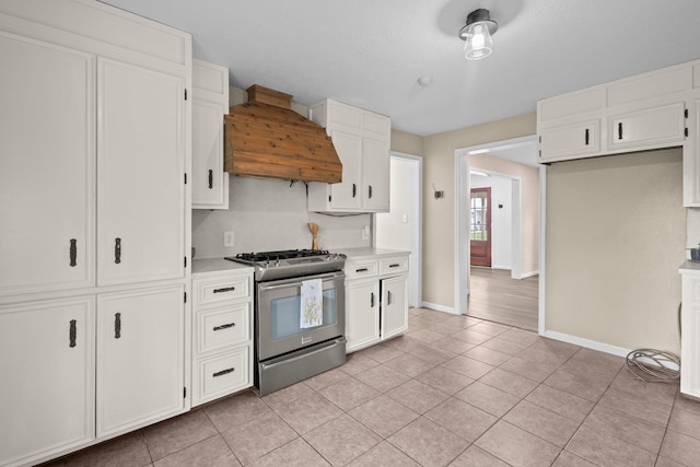 kitchen with light countertops, baseboards, gas range, custom exhaust hood, and white cabinetry