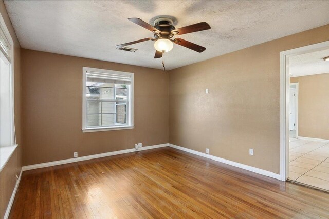 empty room with ceiling fan, a textured ceiling, and light wood-type flooring