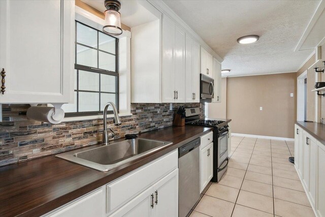 kitchen featuring sink, a textured ceiling, light tile patterned flooring, white cabinetry, and stainless steel appliances