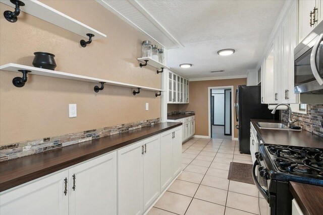 kitchen with wooden counters, sink, black appliances, white cabinets, and light tile patterned flooring