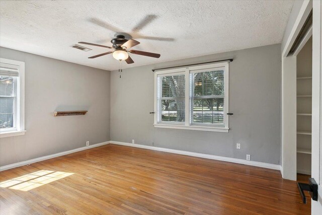 unfurnished room with ceiling fan, wood-type flooring, a textured ceiling, and a wealth of natural light