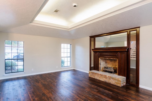 unfurnished living room featuring dark wood-type flooring, a tray ceiling, and a brick fireplace