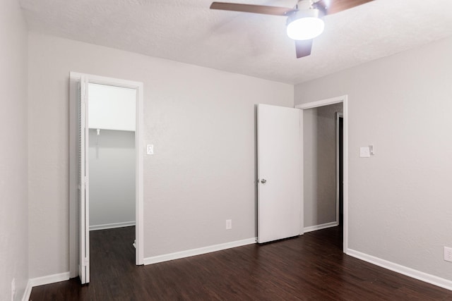 unfurnished bedroom with a spacious closet, dark wood-type flooring, a closet, and ceiling fan