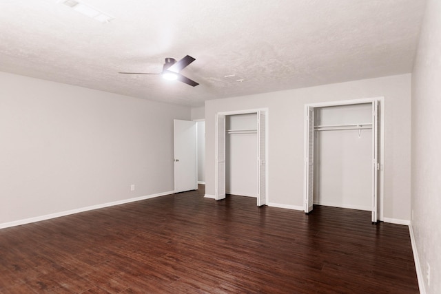 unfurnished bedroom featuring two closets, a textured ceiling, dark hardwood / wood-style floors, and ceiling fan