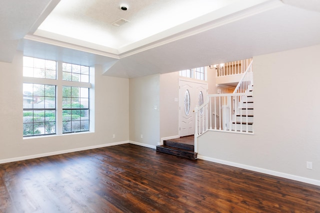 unfurnished living room with dark wood-type flooring, a raised ceiling, and an inviting chandelier