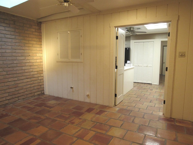 unfurnished room featuring a ceiling fan, a skylight, brick floor, and brick wall