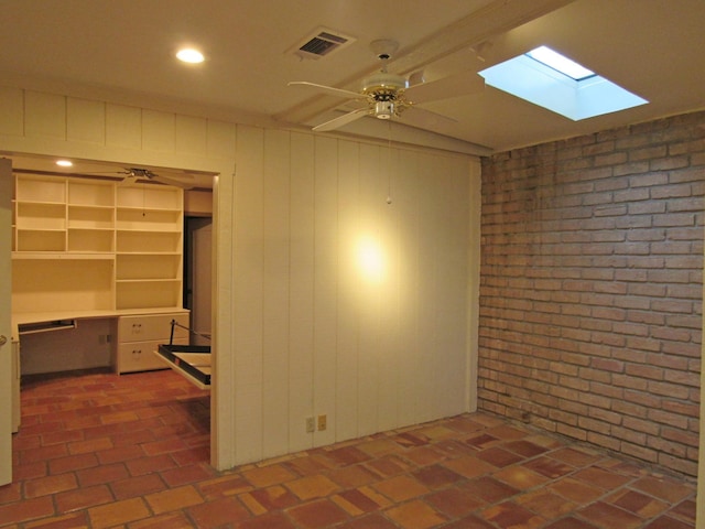 spare room featuring visible vents, built in study area, brick wall, ceiling fan, and brick floor