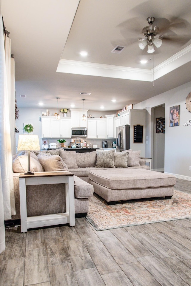 living room with ornamental molding, ceiling fan, and a tray ceiling