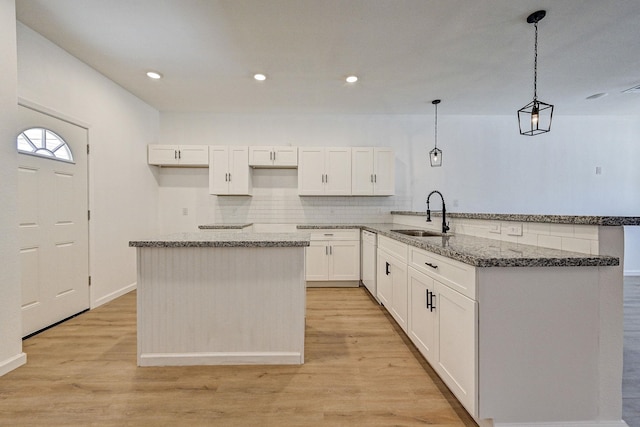 kitchen featuring kitchen peninsula, light wood-type flooring, sink, decorative light fixtures, and white cabinets