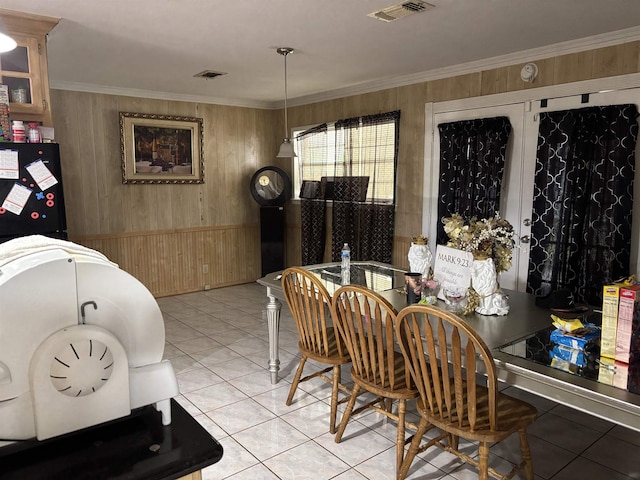 dining room featuring crown molding, light tile patterned flooring, wood walls, and visible vents