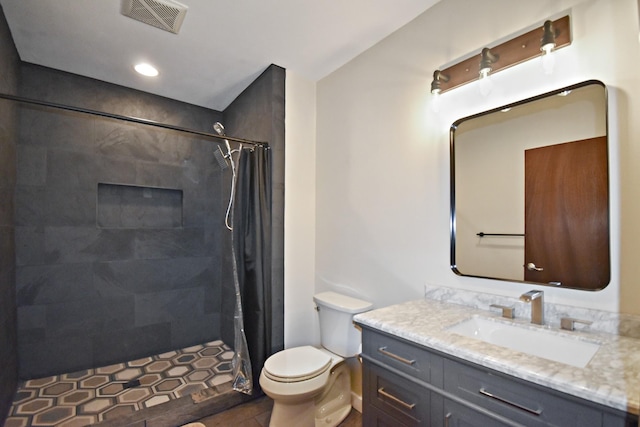 bathroom featuring vanity, toilet, visible vents, and a tile shower