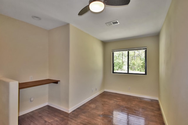spare room with dark wood finished floors, visible vents, a ceiling fan, and baseboards