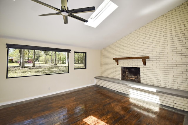 unfurnished living room with a ceiling fan, lofted ceiling with skylight, a brick fireplace, and wood finished floors