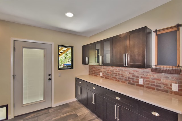 kitchen with glass insert cabinets, baseboards, dark brown cabinetry, light countertops, and a barn door
